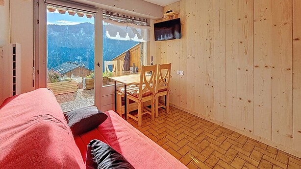 Een gezellige kamer met een rode bank, houten vloer en een televisie aan de wand.