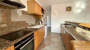 Una cocina con encimeras de granito, armarios de madera, una campana extractora de acero inoxidable y un microondas.
