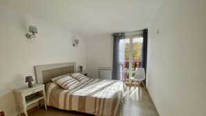 Un dormitorio con cama, mesitas de noche, una silla y una ventana con cortinas.