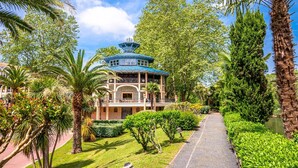 Un edificio de estilo tradicional con techo azul, rodeado de exuberante vegetación y palmeras.