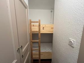 Quarto pequeno e estreito com uma beliche, uma porta e um interruptor de luz na parede.