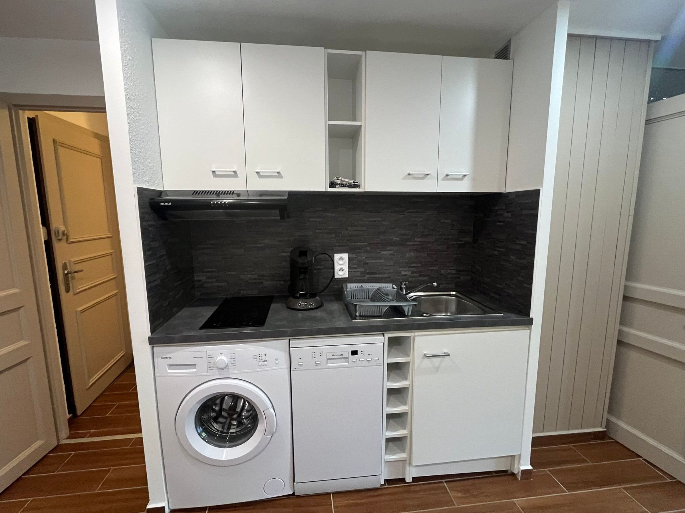 A compact kitchen with a built-in washer and dryer, a sink, and a coffee maker.