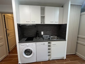 Cozinha compacta com máquina de lavar e secar integradas, pia e cafeteira.