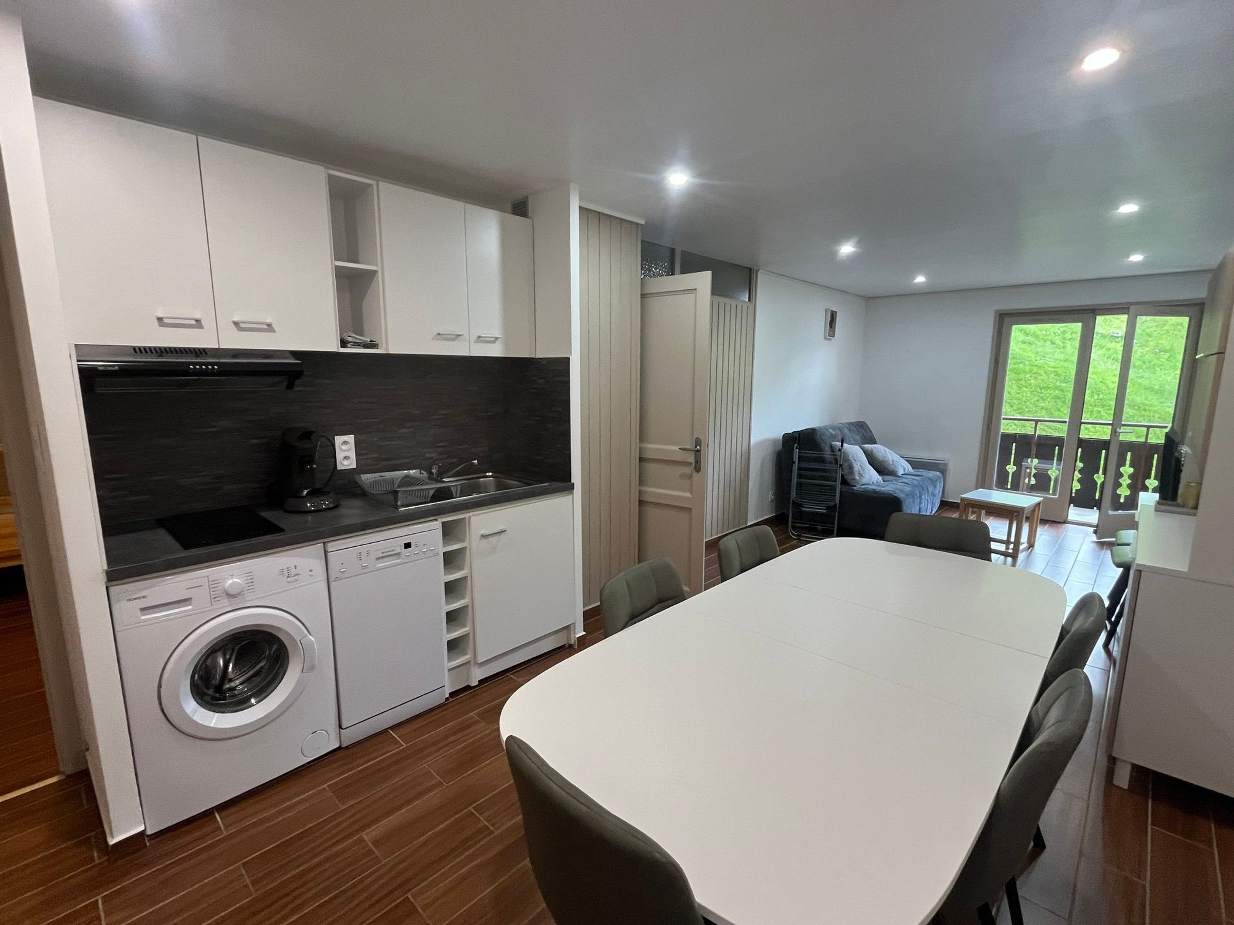 A modern kitchen with a built-in washing machine, a dining area with a table and chairs, and a balcony with a view.