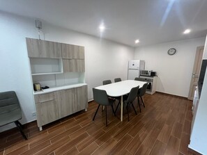 A compact kitchen with a dining area, featuring a white table, grey chairs, and a microwave.