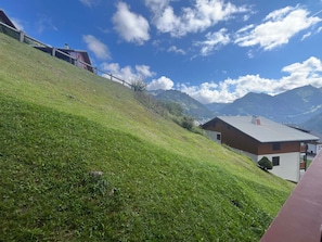 Uma encosta gramada com um edifício de madeira e uma construção vermelha ao fundo.