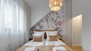 A hotel room with a large bed, two pillows, a nightstand, a lamp, and a floral wallpaper. - Waterlane Vintage Fitness & Parking by Downtown Apartments (Gdansk)