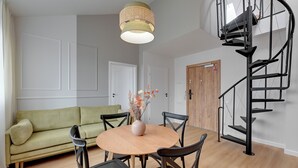 A modern living room with a round wooden table, black chairs, a green sofa, and a spiral staircase. - Waterlane Vintage Fitness & Parking by Downtown Apartments (Gdansk)