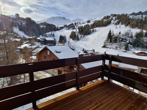 A wooden deck with a view of a snow-covered mountain landscape, including houses and a ski resort.
