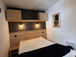 Un dormitorio pequeño y acogedor con cabecera de madera, dos lámparas de noche, un ventanal y un banco al pie de la cama.