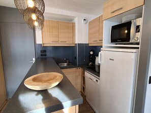 A modern kitchen with wooden cabinets, a black countertop, a microwave, a coffee maker, and a wooden cutting board.