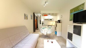 Um espaço compacto com sofá, mesa de jantar e cadeiras, cozinha e televisão.