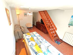 Ein Essbereich mit einem langen Tisch, der für vier Personen gedeckt ist, einer Couch, einem Sessel, einem Schrank und einer Treppe.