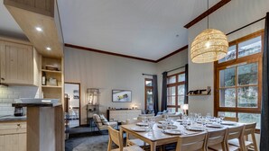 Une cuisine moderne avec des meubles en bois, un coin repas doté d’une table ronde pour six personnes et de grandes fenêtres offrant une vue sur l’extérieur.