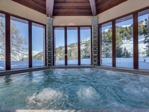 A spa area with a hot tub, large windows, stone pillars, and a snowy mountain view.