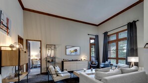 Un salon moderne avec un canapé, une table basse et un téléviseur. Il y a également un coin repas avec une table et des chaises. La pièce est dotée de grandes fenêtres avec des rideaux.