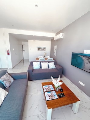 Uma sala de estar moderna com um sofá, mesa de centro e uma TV de tela plana na parede.