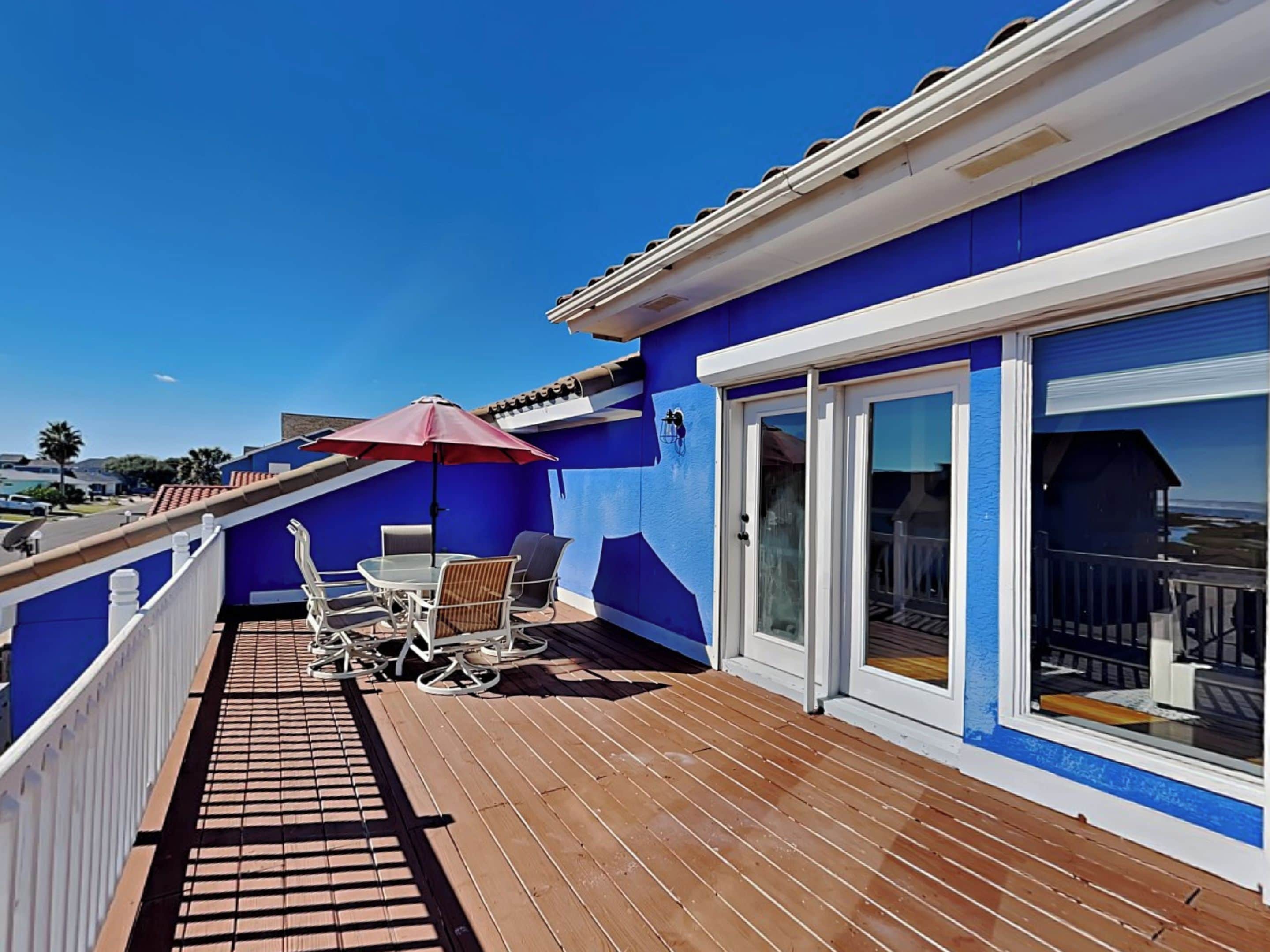 A balcony with a wooden deck, a table with chairs, and a red umbrella.