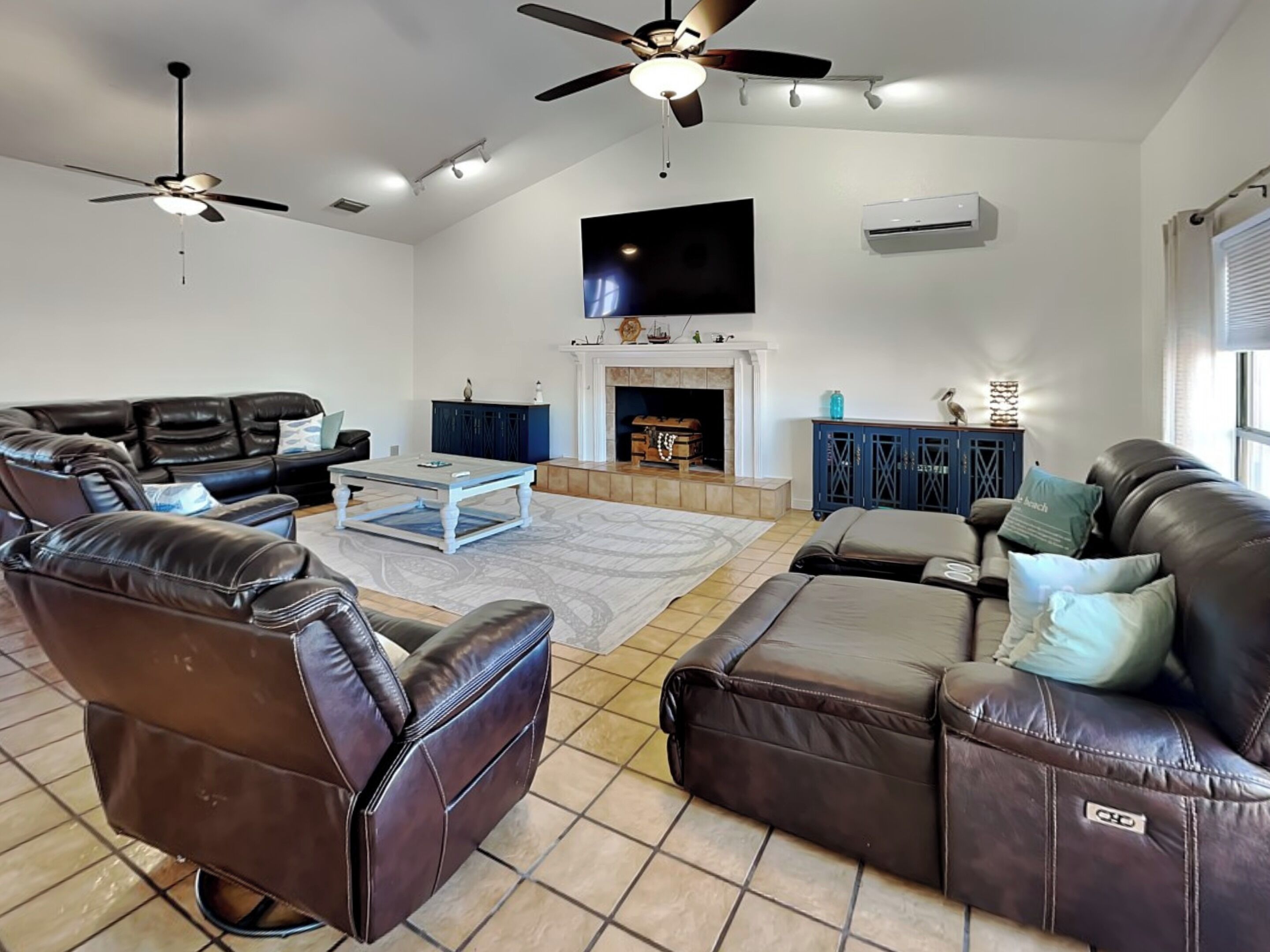 A living room with leather sofas, a coffee table, a fireplace, and ceiling fans.