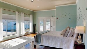 Une chambre à coucher avec un grand lit, une table de chevet, une lampe et une vue sur l’extérieur par une fenêtre.
