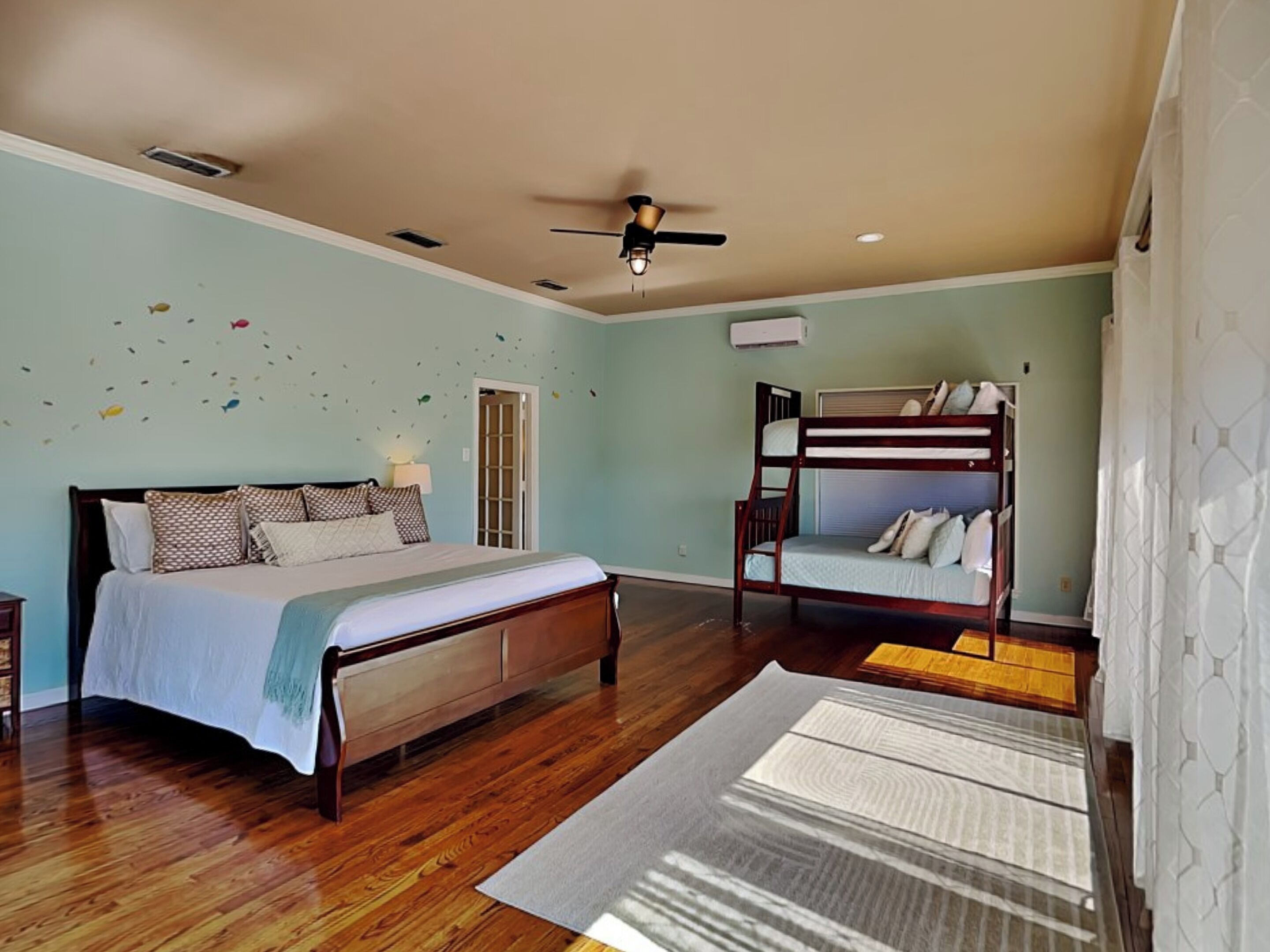 A bedroom with a bed, a bunk bed, wooden flooring, a ceiling fan, and a wall-mounted air conditioner.