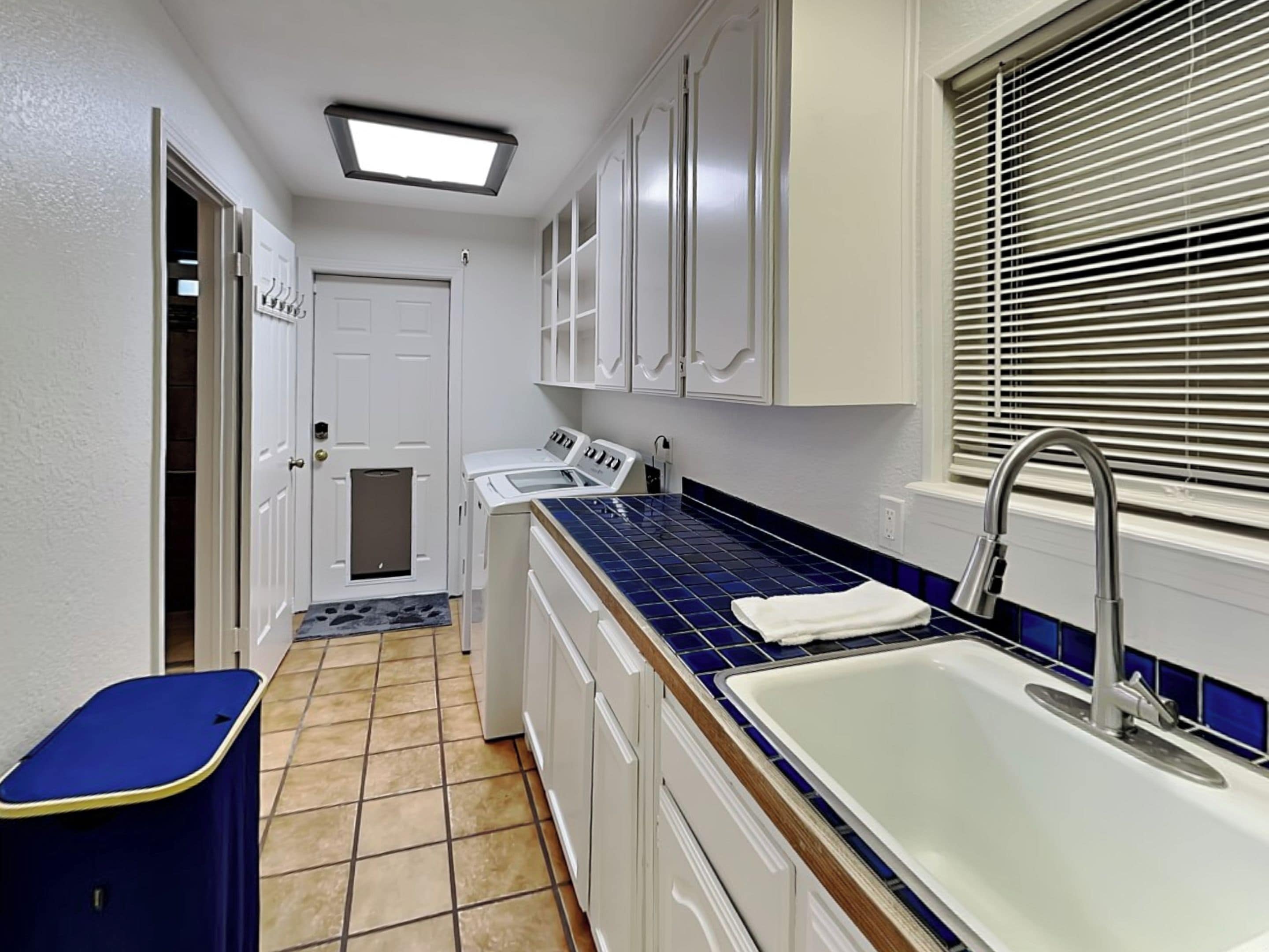 A laundry room with a washing machine, dryer, and a sink with a window above.