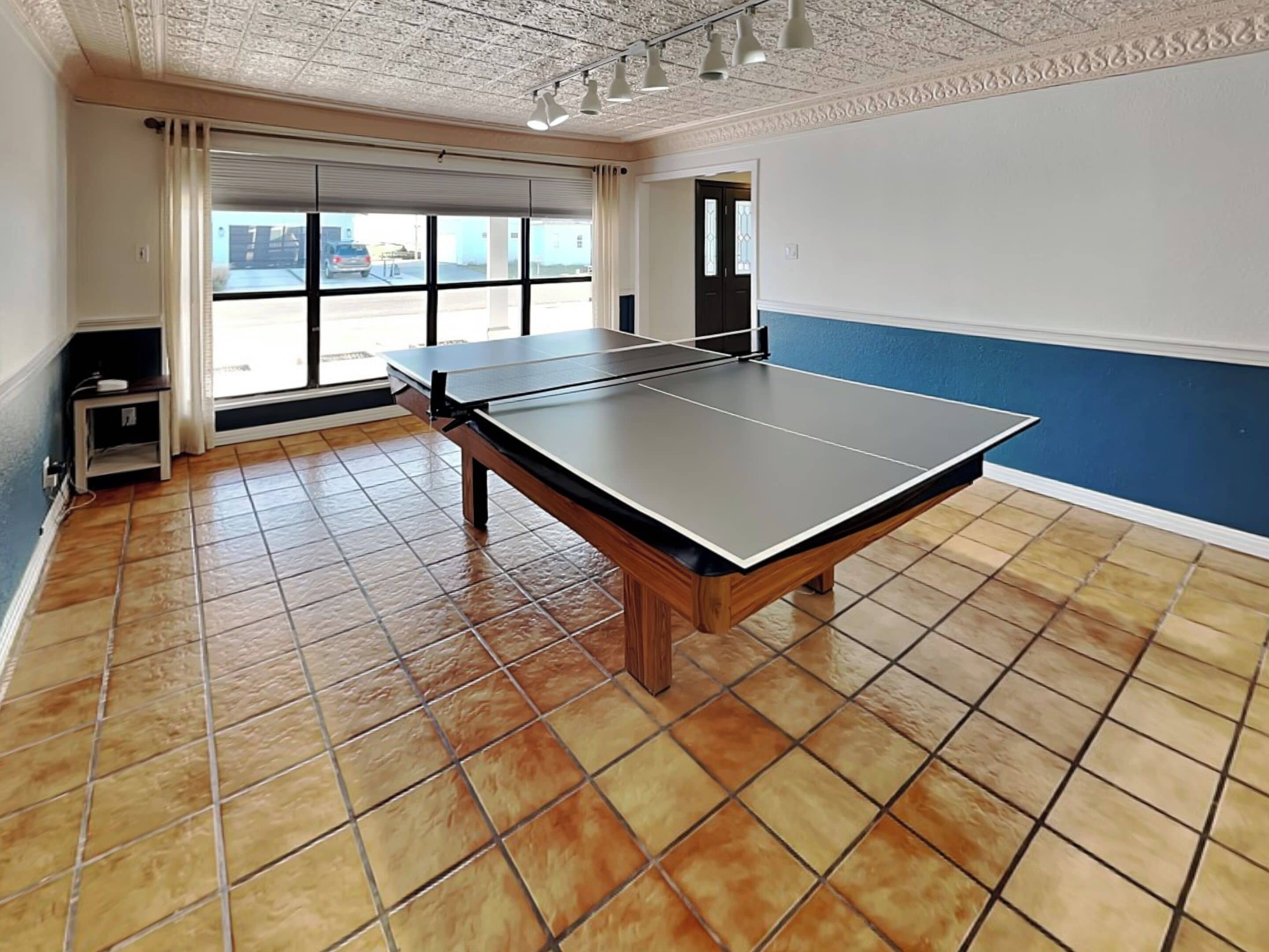 Ein Zimmer mit Tischtennisplatte, großen Fenstern und Blick ins Freie.