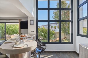 A dining area with a large window, a round table, and black chairs. - Villas Odalys Le Domaine d’Anadara (Anglet)