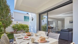 Un comedor al aire libre con una mesa dispuesta para cuatro personas, rodeada de sillas, y vistas al área de estar contigua.