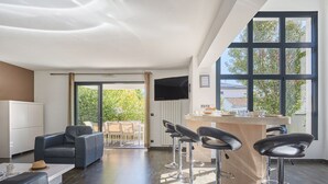 Una sala de estar moderna con un sofá, una mesa de centro y un televisor. Cuenta con una zona de bar con taburetes y una barra.