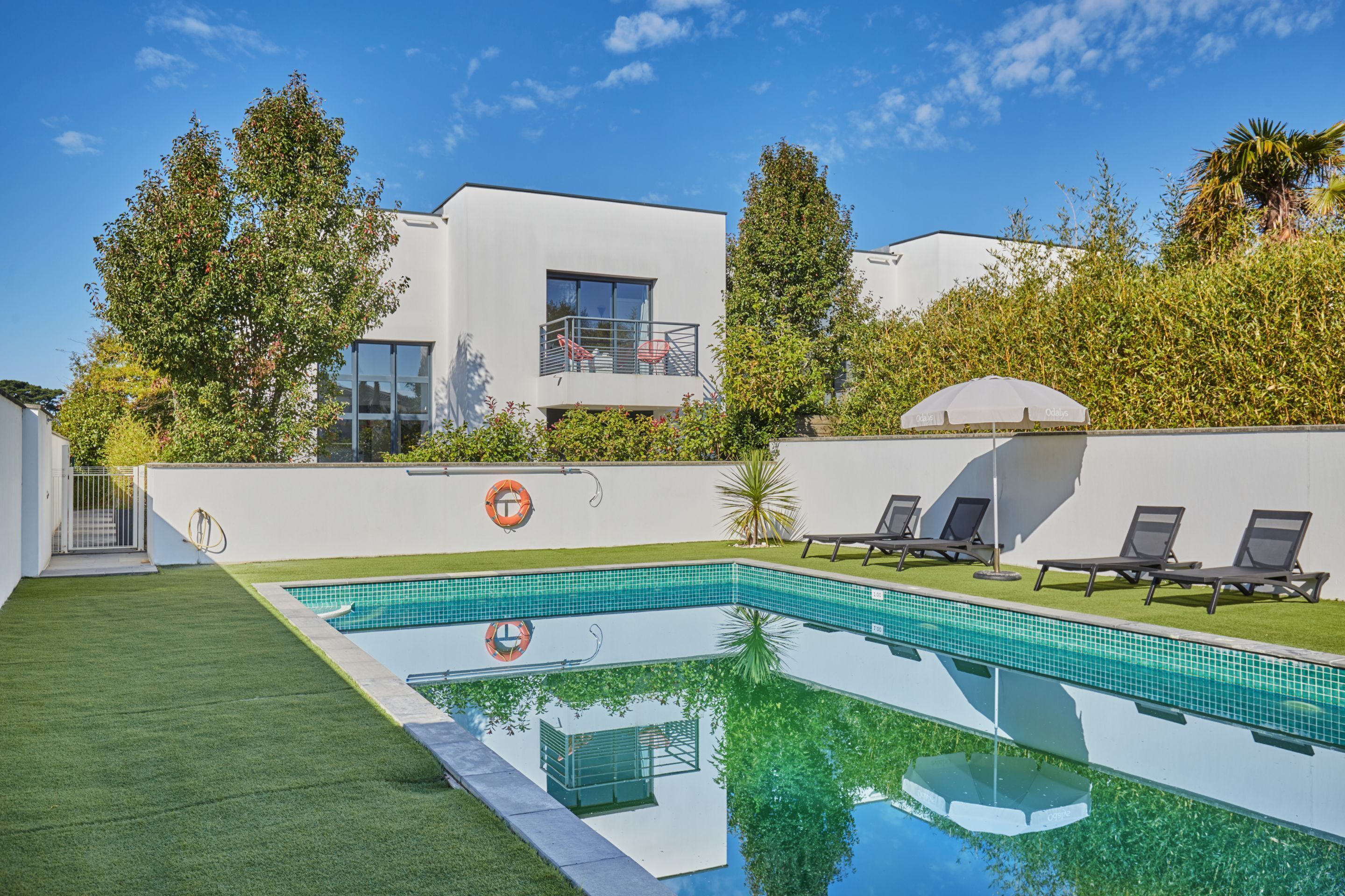 A modern pool area with a clear blue pool, a white building with a balcony, and a grassy lawn.