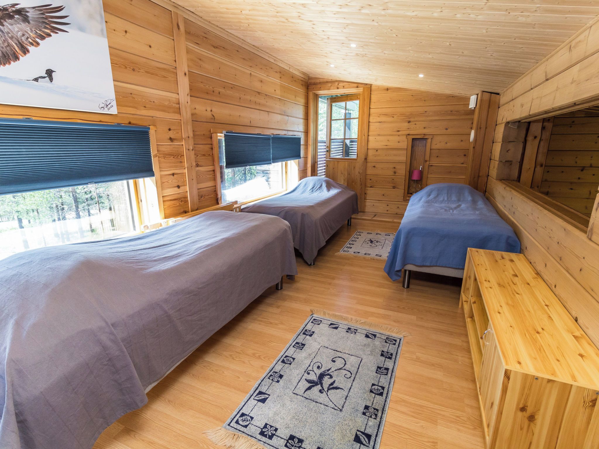 A cabin with two beds, a wooden floor, and a window with blinds.