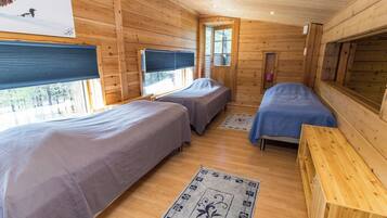 A cabin with two beds, a wooden floor, and a window with blinds.