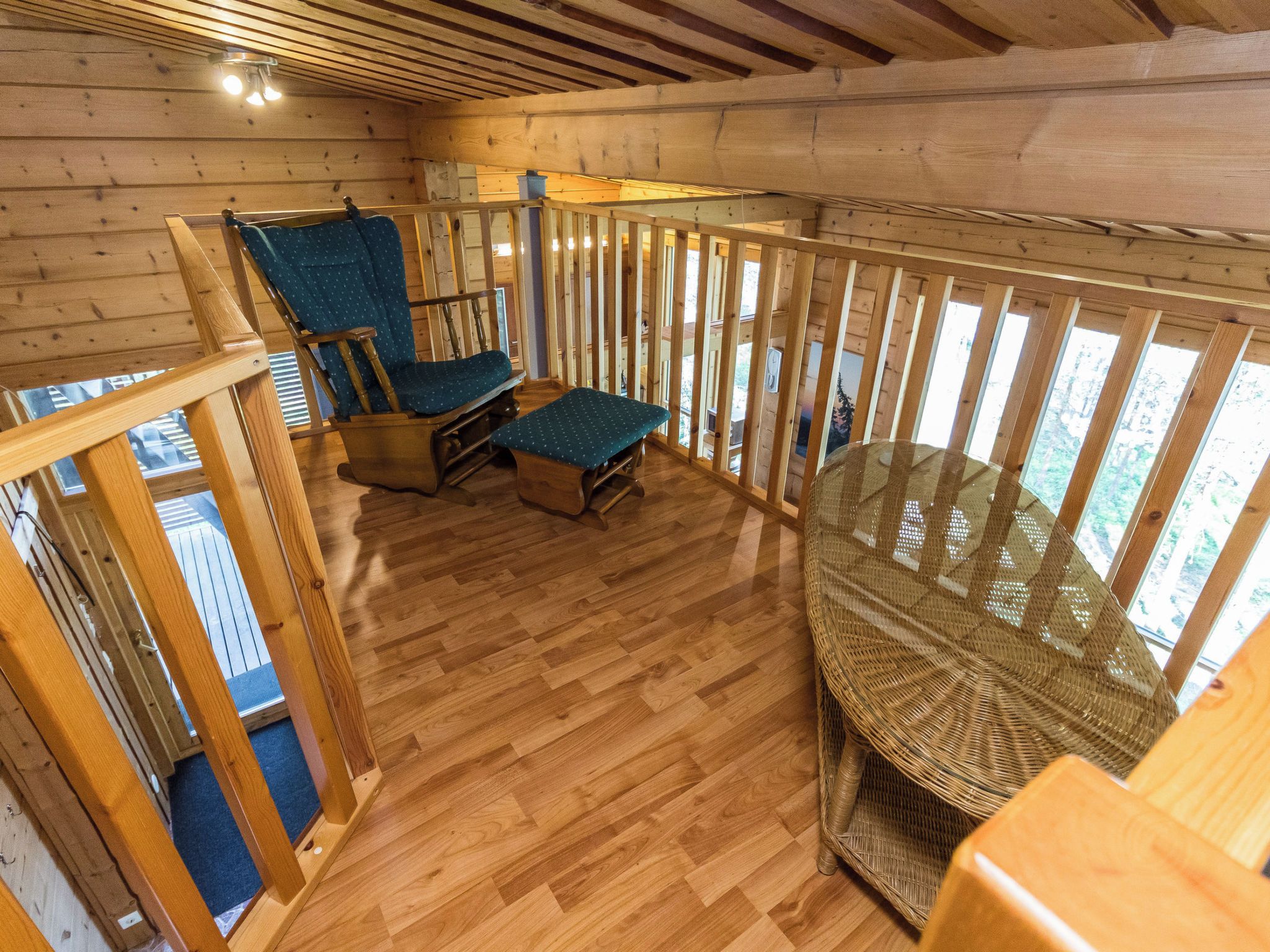 A wooden deck with a glass balustrade, two blue upholstered chairs, and a wicker chair.
