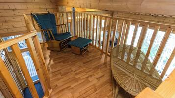 A wooden deck with a glass balustrade, two blue upholstered chairs, and a wicker chair.