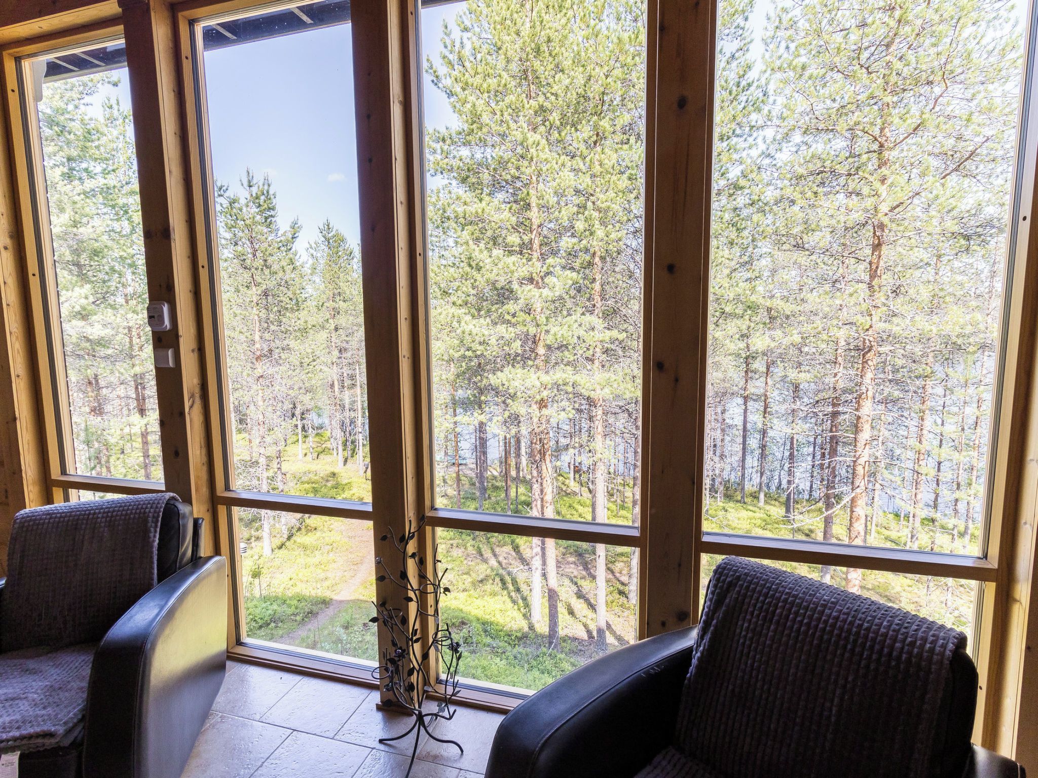 A room with large windows offering a view of a forest. There are two chairs and a small table.