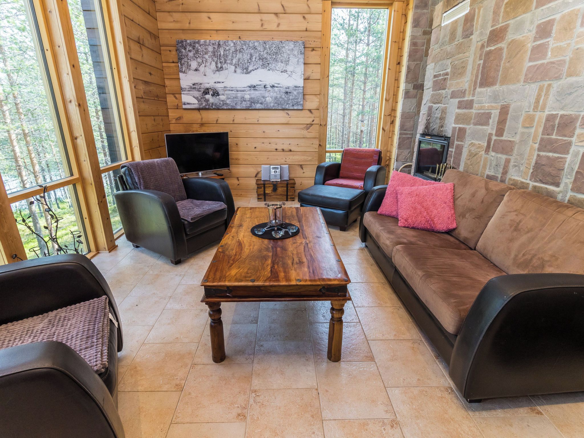 Un interior acogedor con piso de madera, chimenea de piedra y un ventanal con vistas a un bosque.