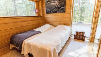 A wooden cabin bedroom with two beds, a painting of rocks, a window, and a view of trees.