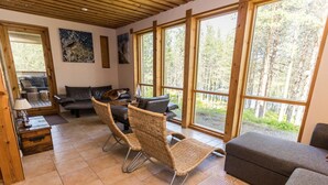 A spacious living area with large windows, a sofa, two wicker chairs, and a coffee table.