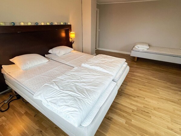 A double bed with a headboard, a bedside table with a lamp, and a bench with a towel.