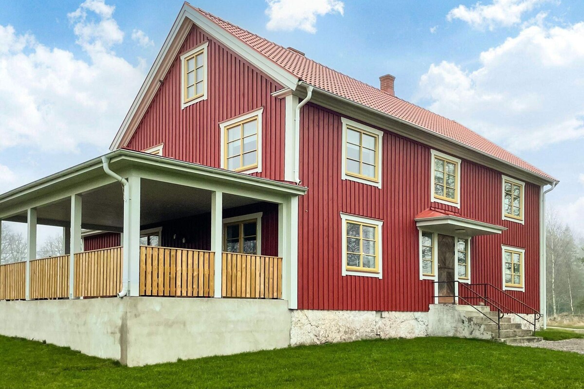A two-story house with a red exterior, a porch with wooden railings, and a stone foundation.
