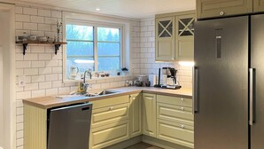 A kitchen with white tiled walls, a wooden countertop, a stainless steel dishwasher, and a refrigerator. - 4 Star Holiday Home in Karlskrona (Eringsboda)