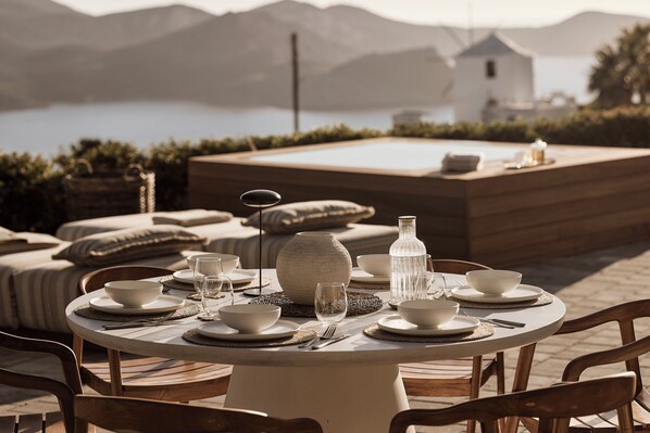 A round table set for dining with a view of mountains and a body of water in the background. - Windmill Karamitsos since 1859 (Milos)