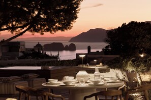 Un comedor con una mesa dispuesta para dos personas, con vistas a un cuerpo de agua y montañas a lo lejos.