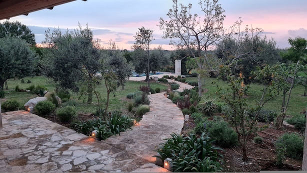 A stone pathway leading through a garden with various plants and trees, surrounded by a natural landscape. - TD Il Faritrullo Trulli in the Itria Valley w Pool (Martina Franca)