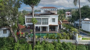 A modern two-story house with a swimming pool, surrounded by lush greenery and palm trees. - Echor Reis Magos Villa Goa (Verem)