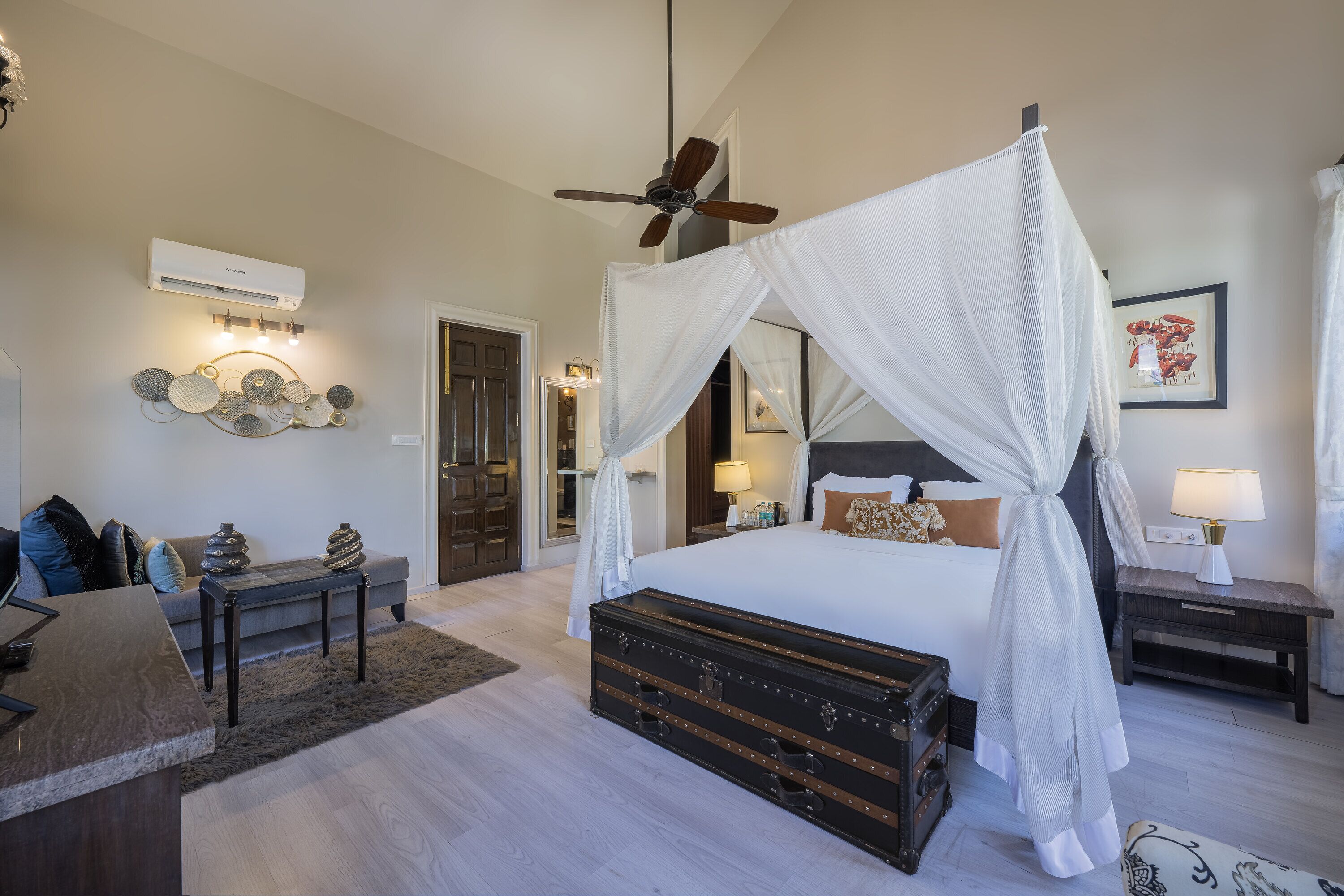 A bedroom with a four-poster bed, a ceiling fan, a bedside table with a lamp, and a large trunk.