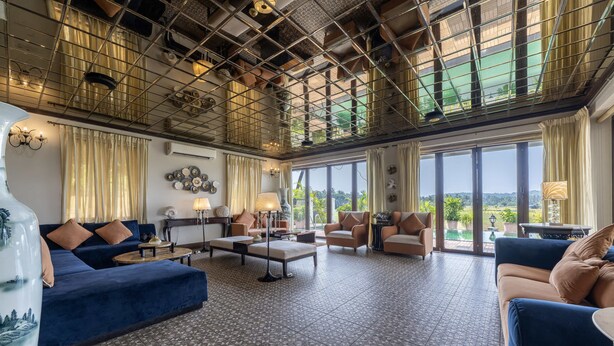 A spacious living area with a high ceiling, large windows, and a variety of seating options including sofas and armchairs. - Echor Reis Magos Villa Goa (Verem)
