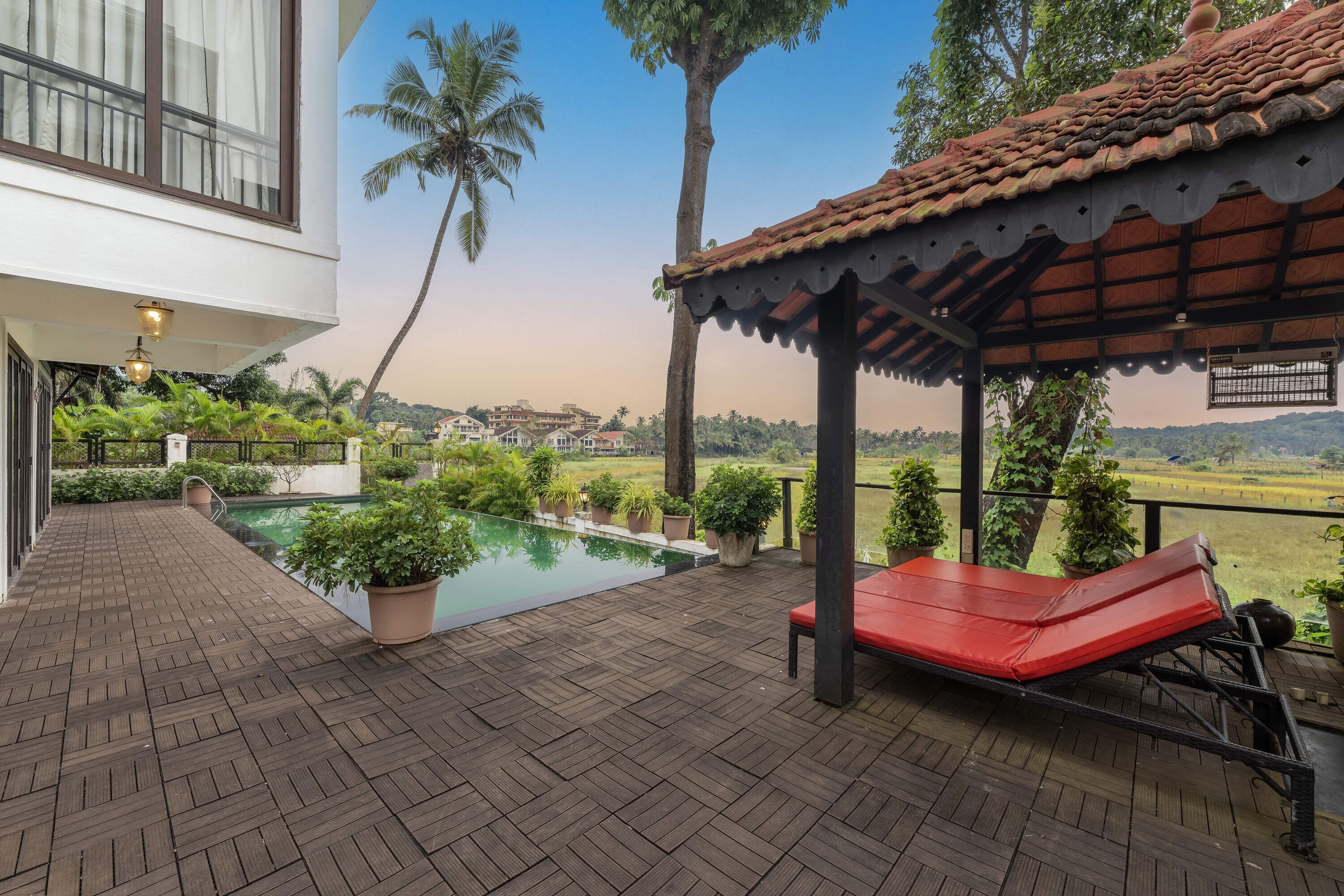 A wooden deck with a pool, a red lounge chair, and a covered seating area with a view of the landscape.