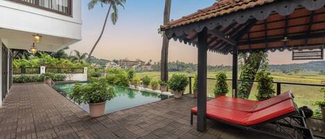 A wooden deck with a pool, a red lounge chair, and a covered seating area with a view of the landscape.
